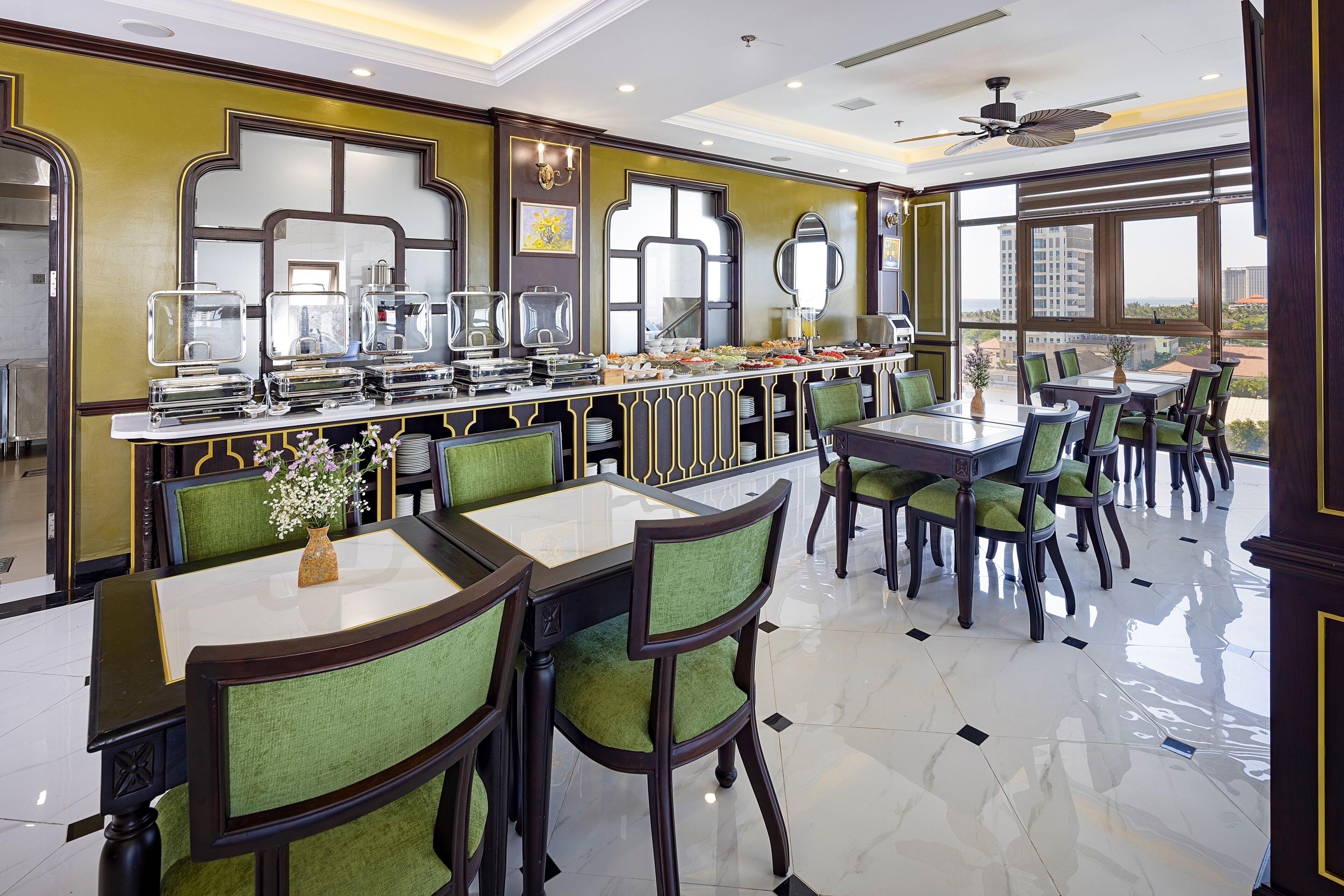 A dining area with a buffet setup, green upholstered chairs, and a ceiling fan.