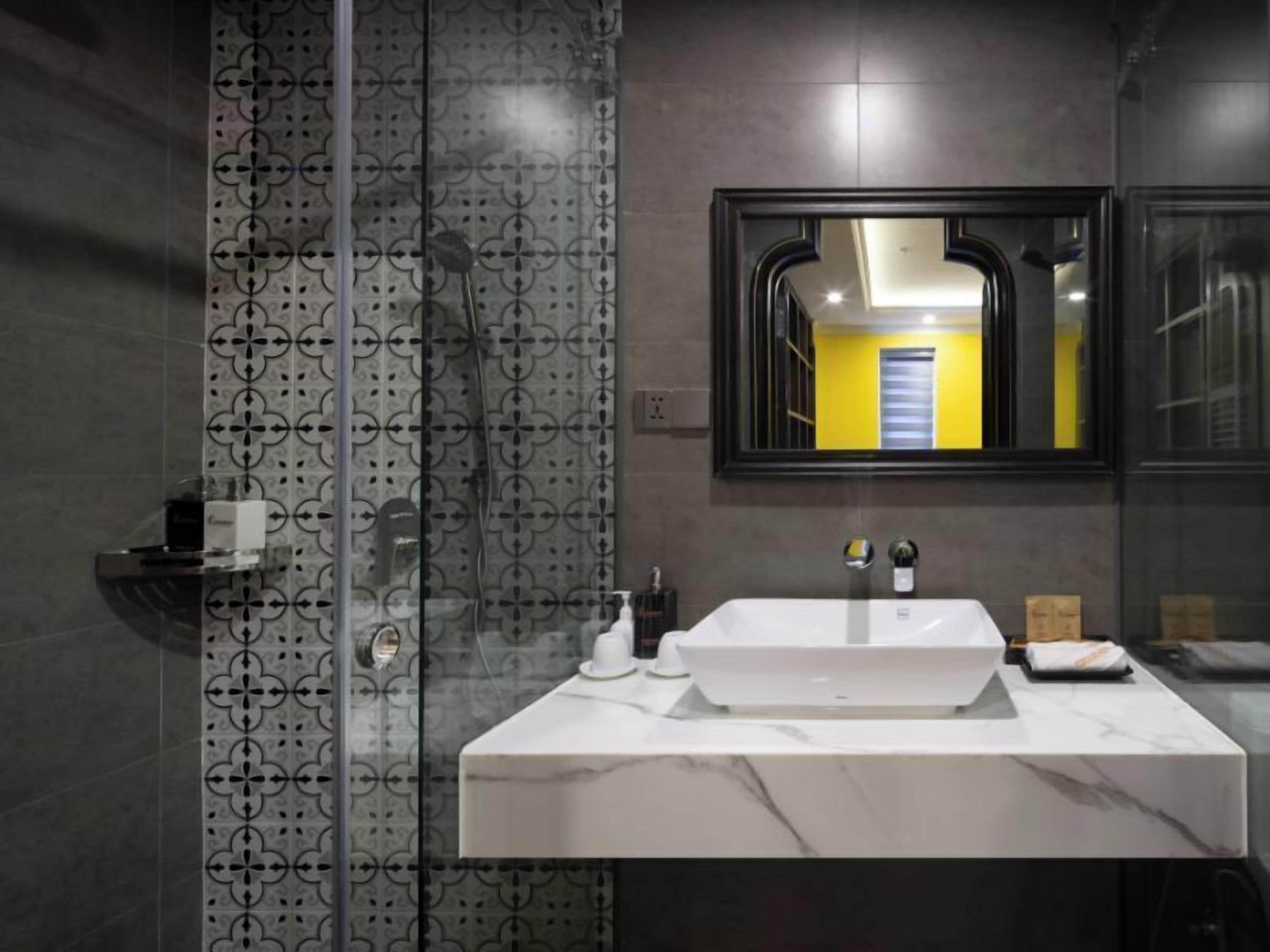 A modern bathroom with a white sink, a glass shower enclosure, and a mirror reflecting a yellow door.