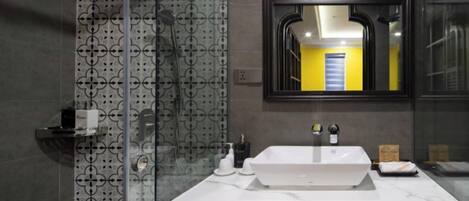 A modern bathroom with a white sink, a glass shower enclosure, and a mirror reflecting a yellow door.