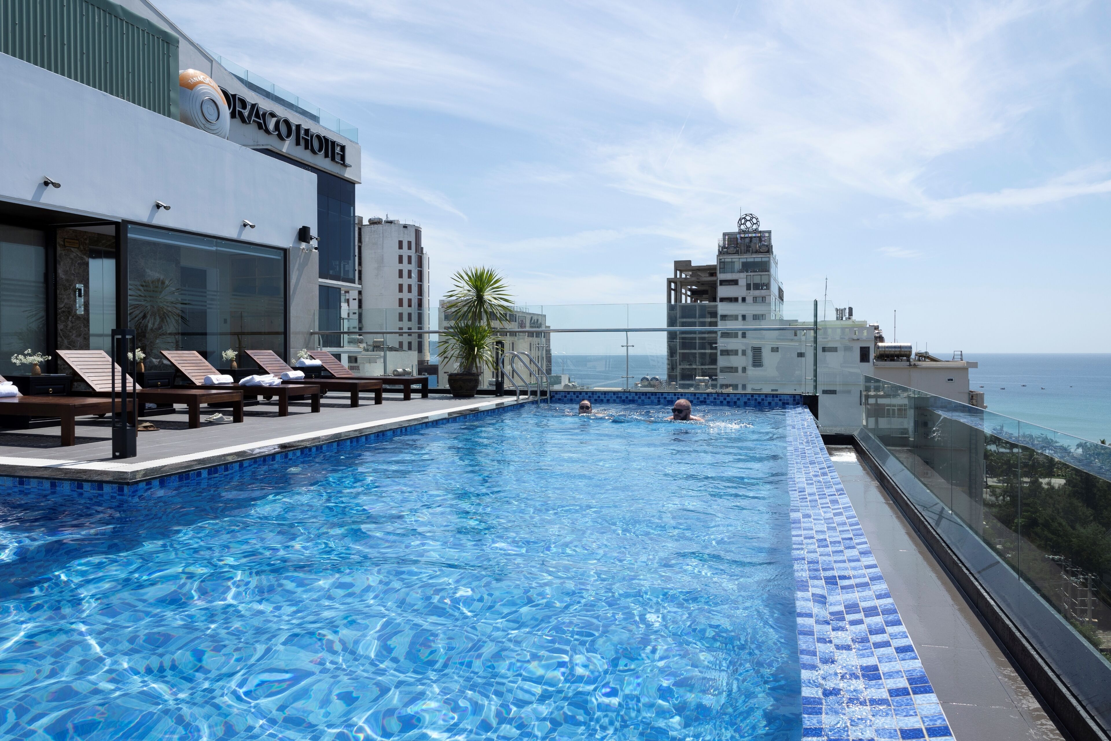 Una piscina infinita en la azotea con sillones de descanso y vistas al océano.