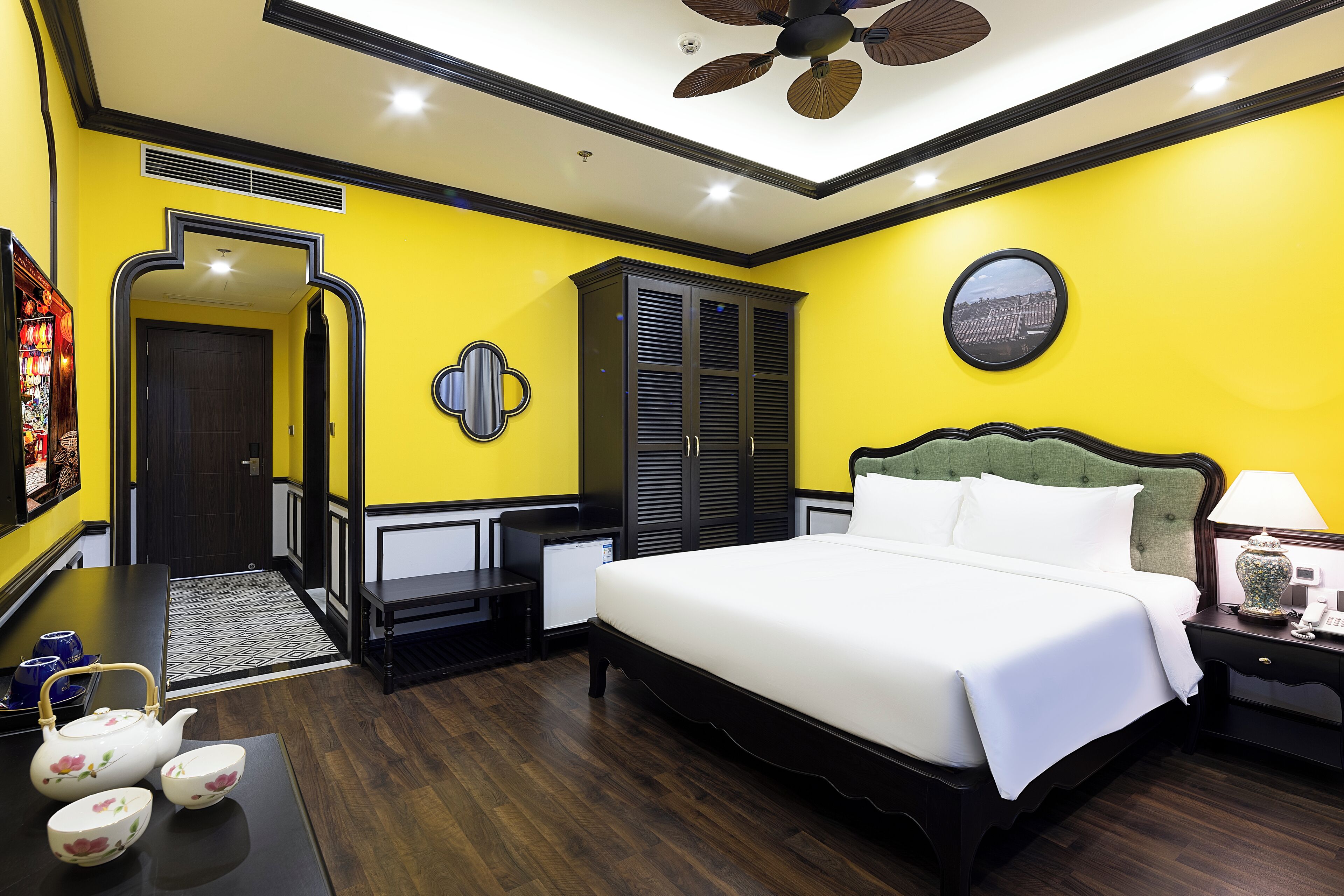 Une chambre d’hôtel avec un grand lit, une table de chevet avec une lampe, une armoire et une petite table avec une théière et des tasses.