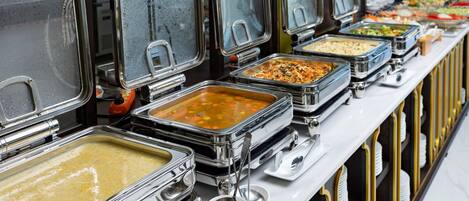 A buffet line with multiple self-service food stations, each with a covered serving tray and a spoon.