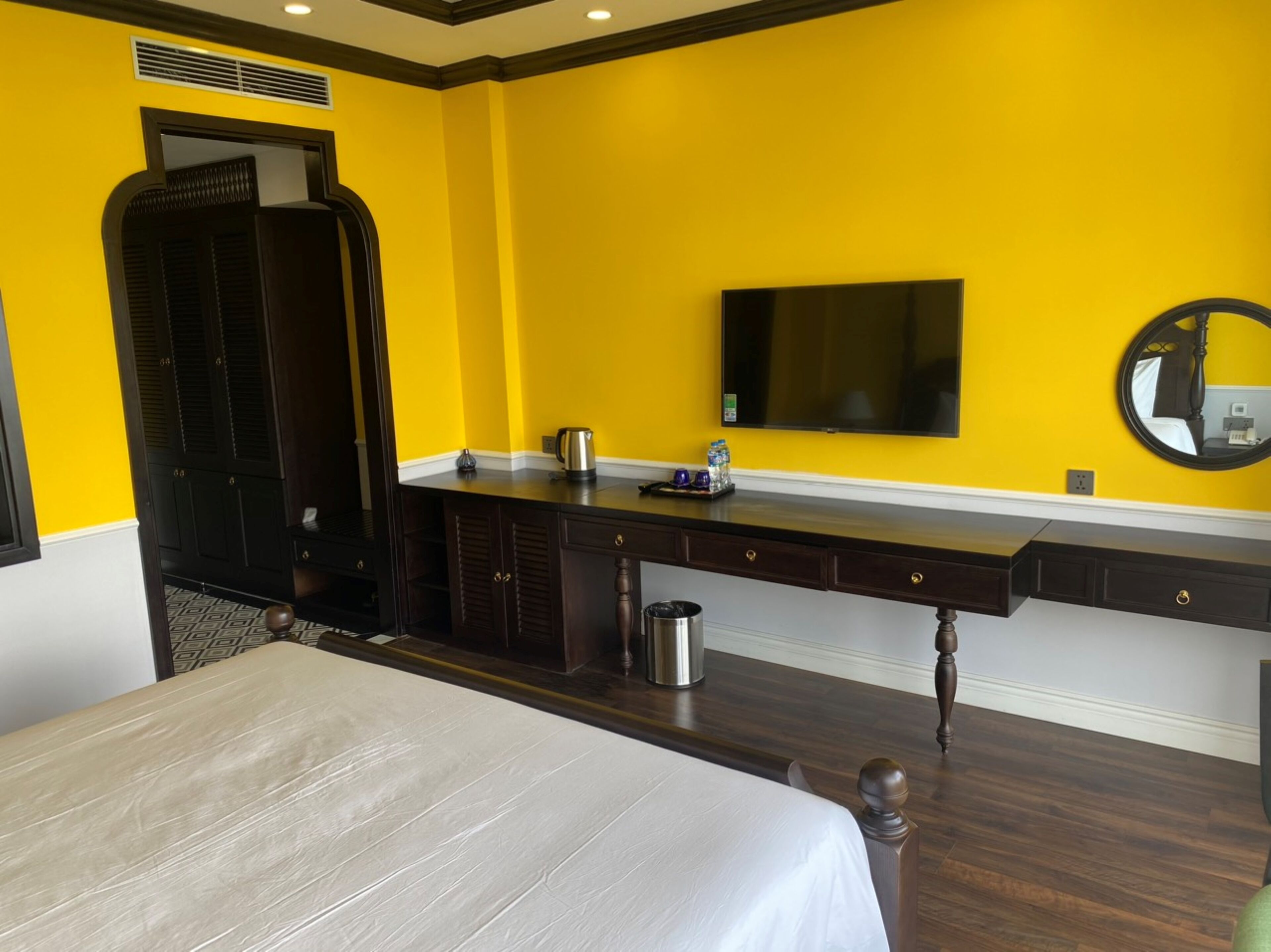 A hotel room with a bed, a desk with a mirror, a television, and a wardrobe.