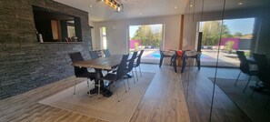 Enjoy meals in this stylish dining area with a long table and comfortable seating, surrounded by a beautiful view of the outdoor pool and patio.
