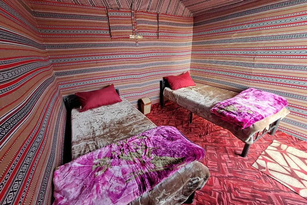 A room with two beds, each with a patterned bedspread and a red pillow. The room has a patterned carpet and a red and beige floor.