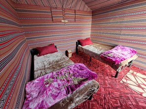 Una habitación con dos camas, cada una con una colcha estampada y una almohada roja. La habitación tiene una alfombra estampada y un suelo rojo y beige.