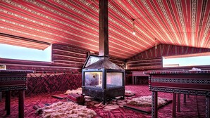 Una habitación tradicional con techo de color rojo estampado, una estufa de leña en el centro y alfombra roja con motivos.