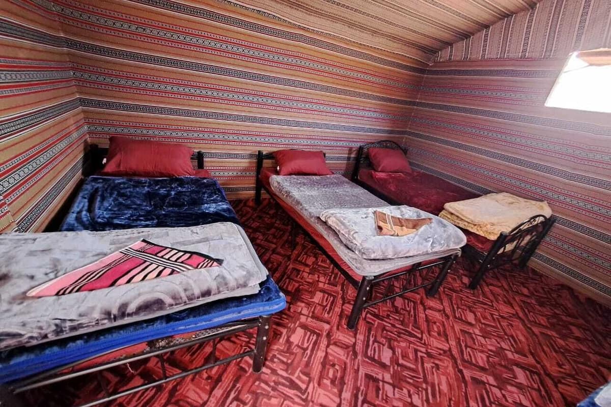A room with three beds, each with a different colored blanket. The room has a patterned carpet and a sloped ceiling.