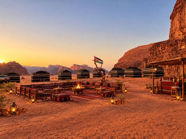 A desert campsite with tents, a fire pit, and a flag.