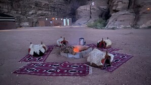 Campaamento en el desierto con tiendas de campaña, una fogata y un paisaje rocoso.