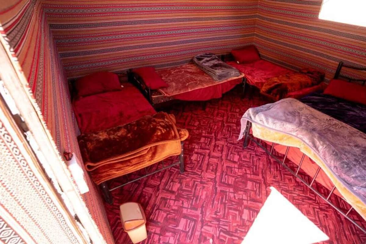 A room with three beds, each with a red and purple blanket, and a patterned carpet.