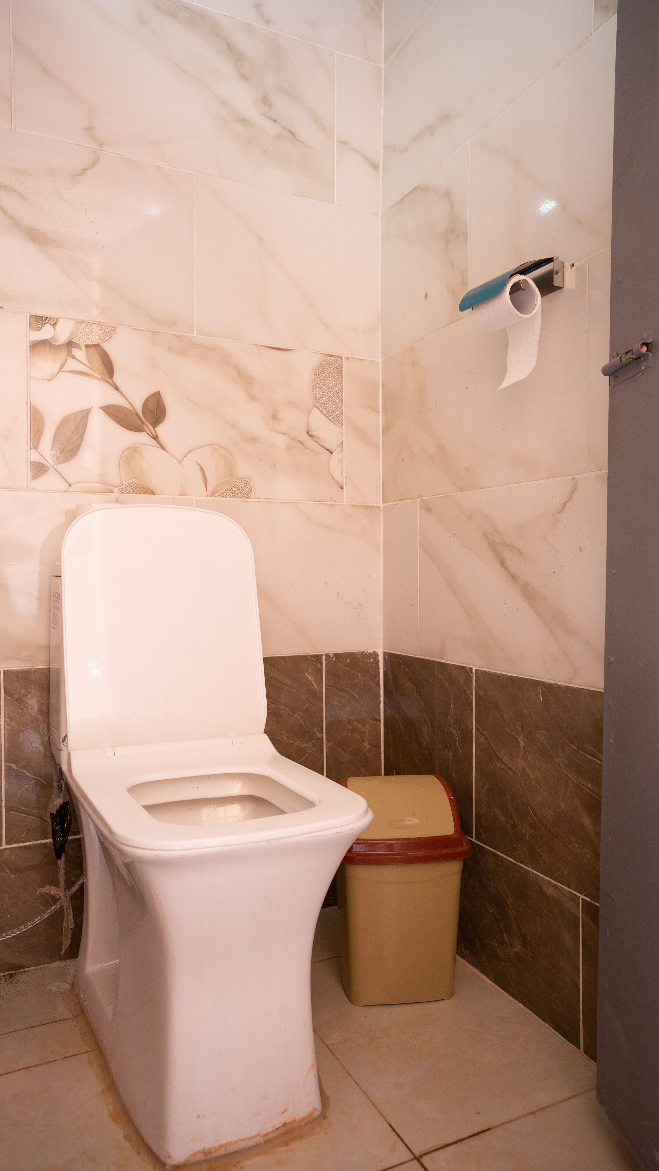 A bathroom with a toilet, a trash bin, and a toilet paper holder on the wall.