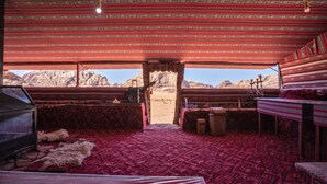 Una habitación con alfombra roja estampada, un armario de madera, un manto de piel y vistas a un paisaje montañoso a través de un umbral abierto.