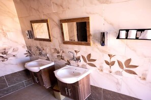 Un baño con dos lavabos, armarios de madera, azulejos de mármol y adornos en la pared con motivos de hojas.