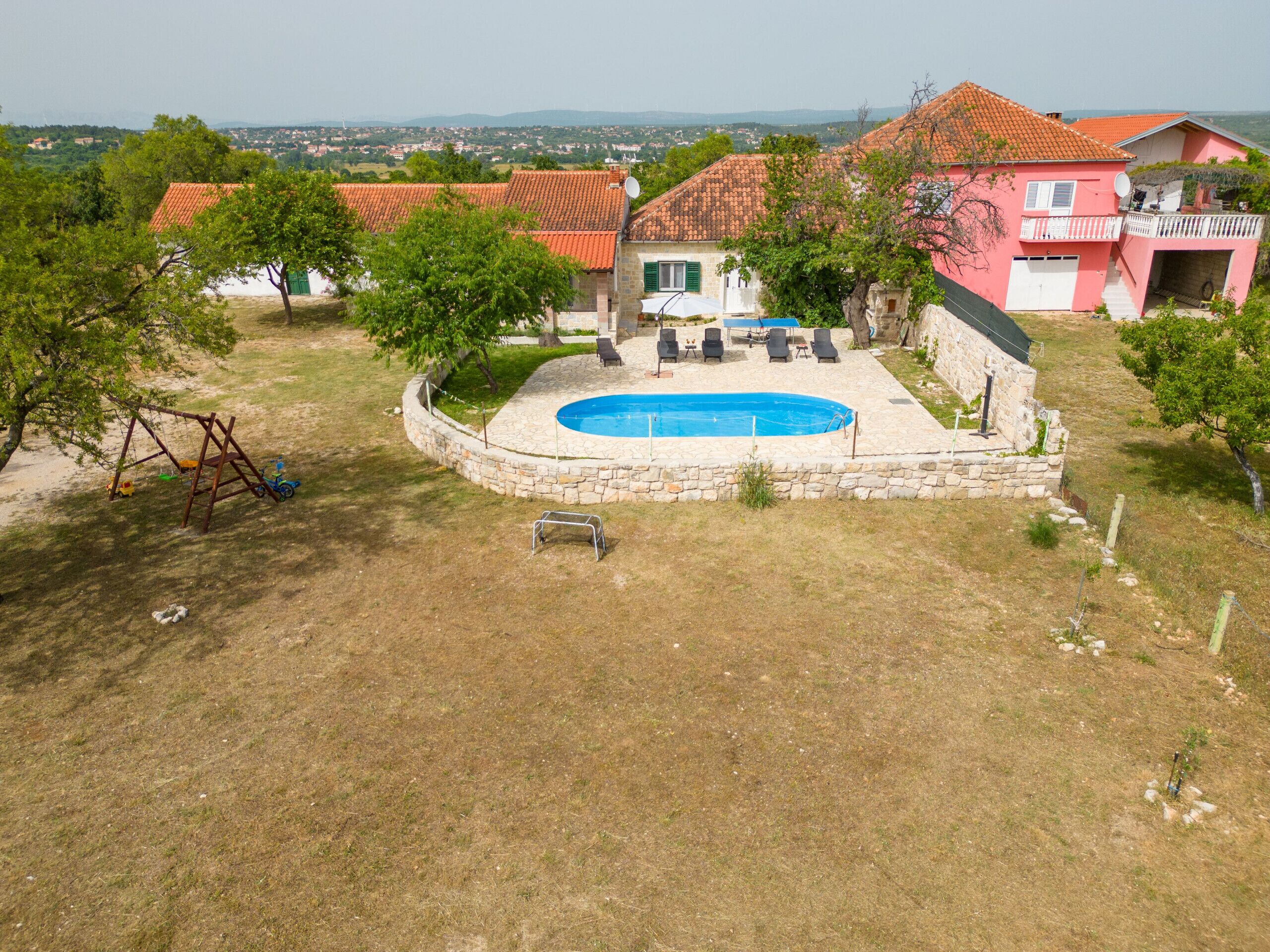 A residential property with a swimming pool, a stone patio, and a swing set.