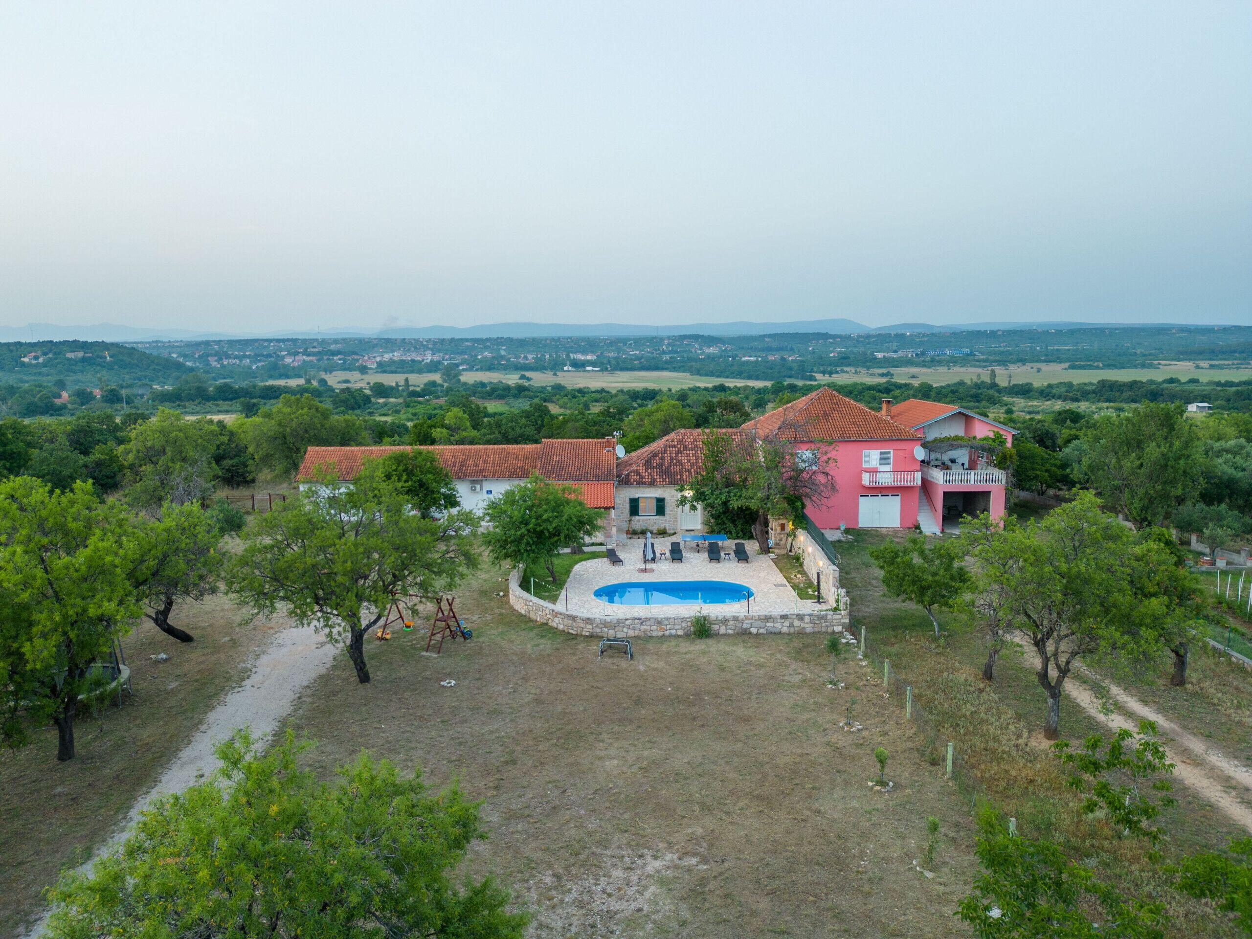 Une grande maison avec une piscine, entourée d’arbres et située dans un cadre rural.