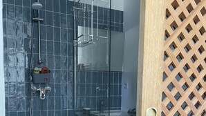 Ein modernes Badezimmer mit Duschkabine aus Glas, einem weißen Waschbecken und einer Holztür mit Gittermuster.