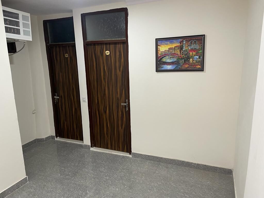 A hallway with two wooden doors, a painting on the wall, and a ceiling vent.