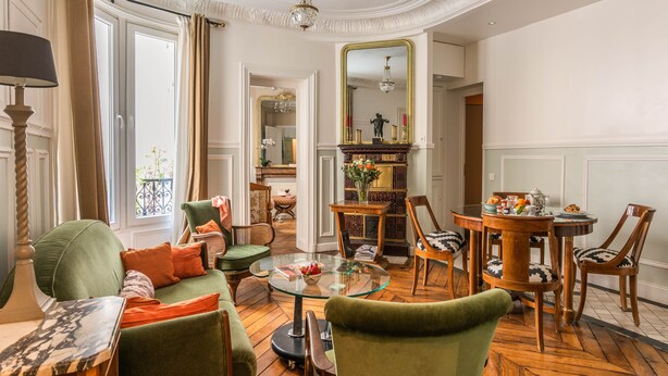 A well-lit room with a green sofa, a round glass table, and a dining area with wooden chairs. - New Paris Centre Historic Marrais Montorgueil Chic Suite Familiale 2 Bedrooms (Paris)
