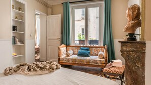 A cozy room with a bed, a sofa with floral upholstery, a bookshelf, and a bust sculpture. - New Paris Centre Historic Marrais Montorgueil Chic Suite Familiale 2 Bedrooms (Paris)
