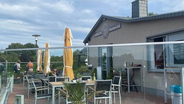 Un espacio al aire libre con mesas, sillas, sombrillas y un edificio con un letrero.