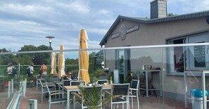 Un espace extérieur aménagé avec des tables, des chaises, des parasols et un bâtiment portant une enseigne.