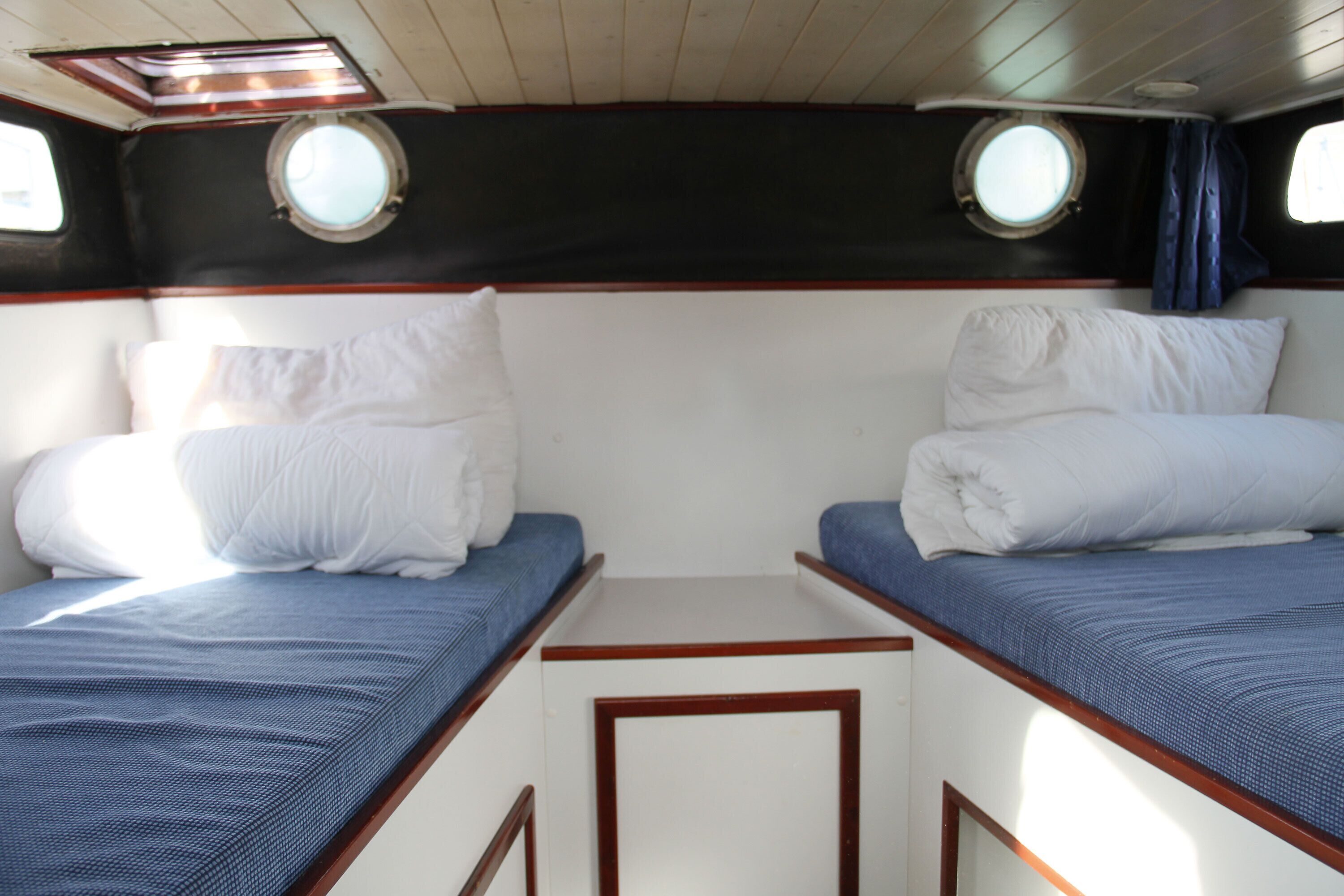Una cabaña con dos camas, cada una con almohada y una manta azul. Hay dos ventanas con cortinas y el techo de la cabaña es de madera.