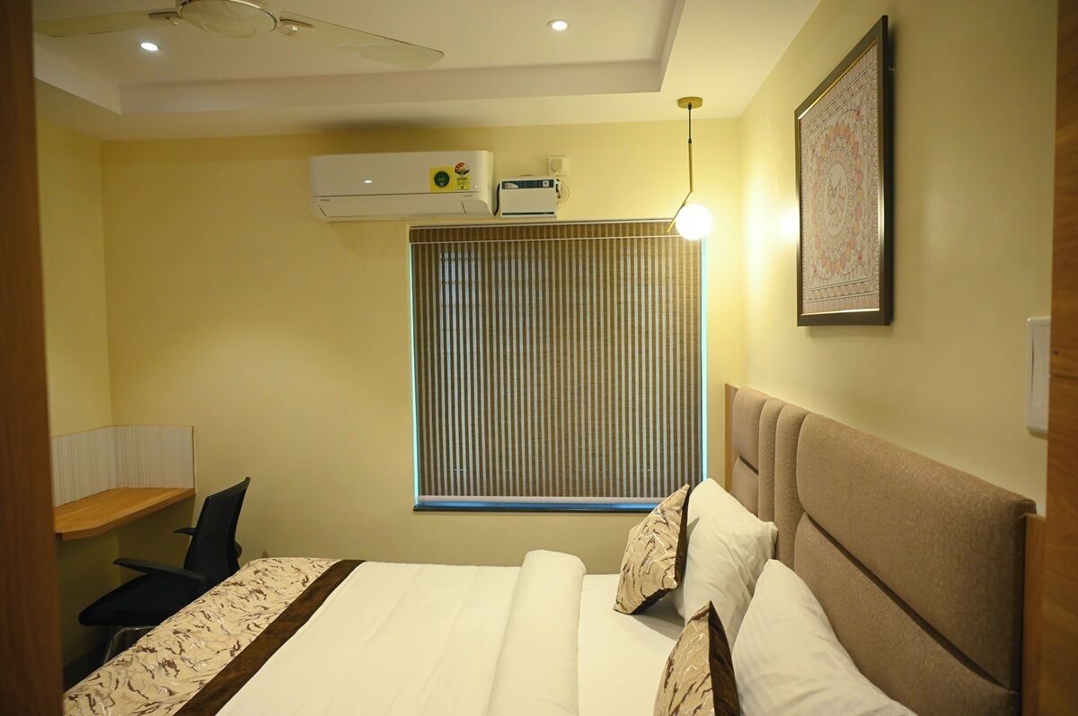 A bedroom with a bed, a desk, and an air conditioning unit.
