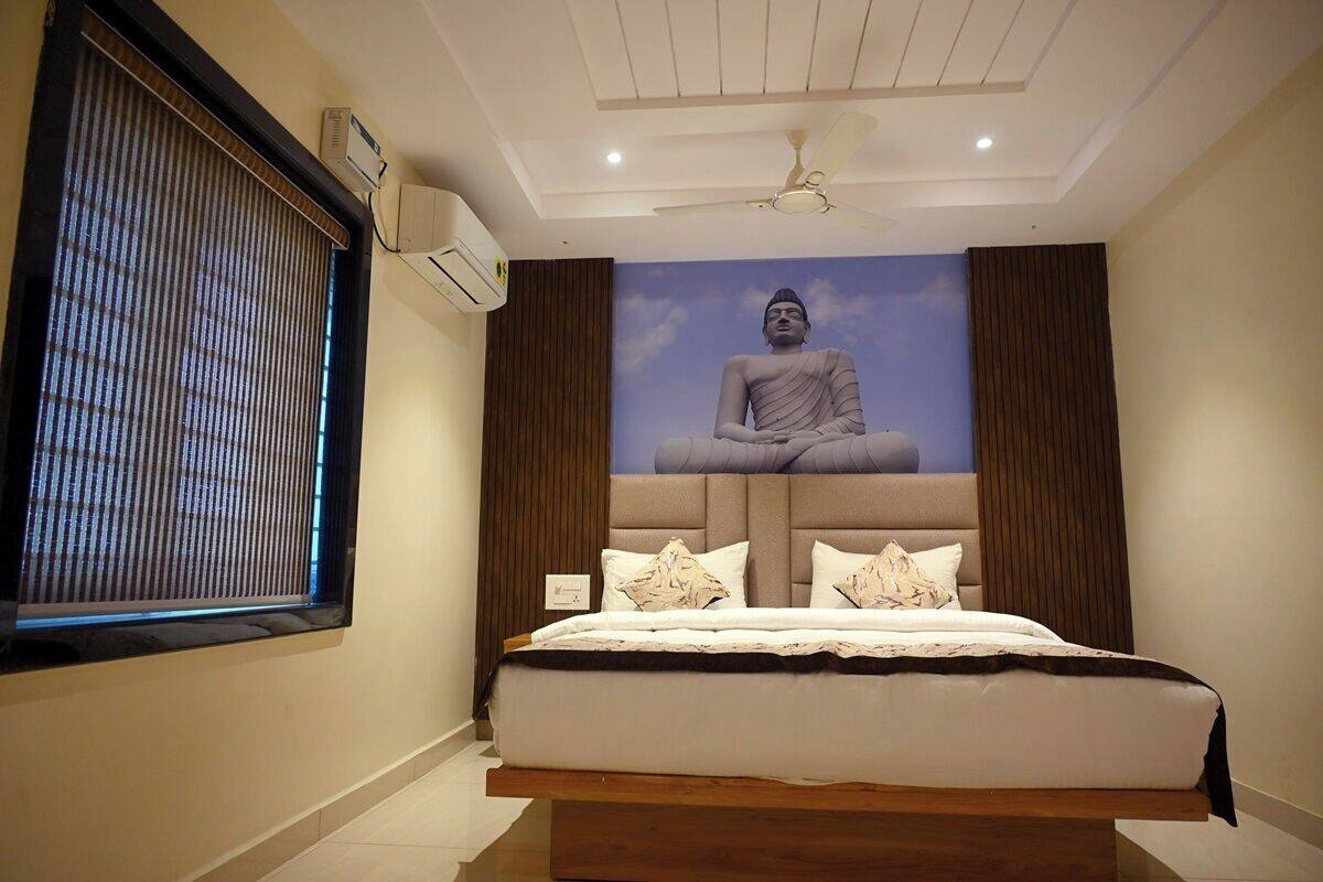 A bedroom with a large bed, a ceiling fan, an air conditioning unit, and a mural of a seated figure on the wall.