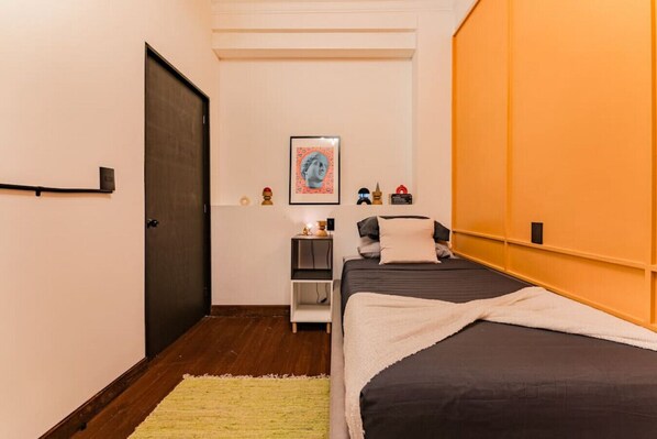 A bedroom with a bed, a nightstand, a framed picture, and a door.