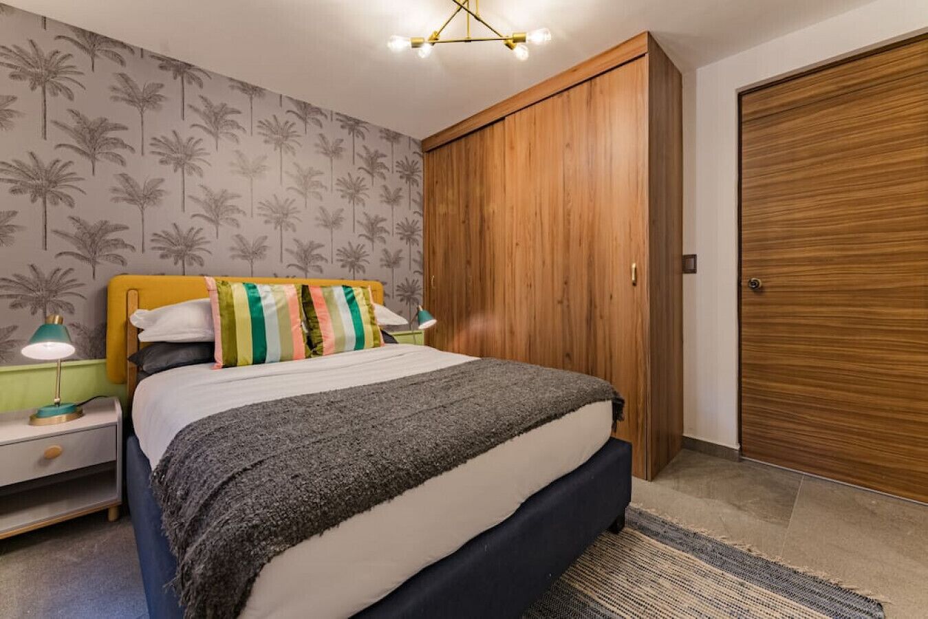 Une chambre à coucher avec un lit, des tables de chevet, une armoire en bois et un mur décoré d’un motif.