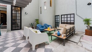 A modern outdoor seating area with a checkered floor, a white sofa, blue chairs, and a beige sofa. - Roma Retreat: Modern Colonial Gem A/C 16 PAX (Ciudad de México)