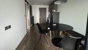 A modern kitchen with a refrigerator, microwave, and sink. There is a dining table with chairs and a pendant light. - 1 bed plus condo near JJ market (Bangkok)