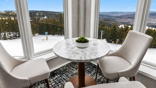A room with a round marble table, two chairs, a potted plant, and a view of a snowy landscape through large windows. - ML115 Lovely Slope Side Getaway Wi-Fi Parking Next to Village (Snowshoe)