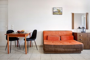 A room with a wooden dining table, two chairs, an orange sofa, a wooden cabinet, and a painting on the wall.