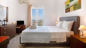 A hotel room with a bed, a desk with a TV, a window with curtains, and a painting on the wall. - Studio Apartment "Yiannis 7" with Sea View, Shared Garden & Wi-Fi (Zakynthos)
