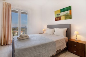 A neatly made bed with a white bedspread, a nightstand with a lamp, and a painting on the wall.