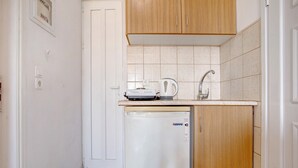 A compact kitchen with a dishwasher, a coffee maker, and wooden cabinets. - Studio Apartment "Yiannis 7" with Sea View, Shared Garden & Wi-Fi (Zakynthos)