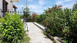 Un chemin menant à un bâtiment doté d’un balcon, entouré de verdure et sous un ciel dégagé.