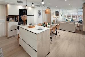 A modern kitchen with a central island, dining area with chairs, and a living room with a sofa.