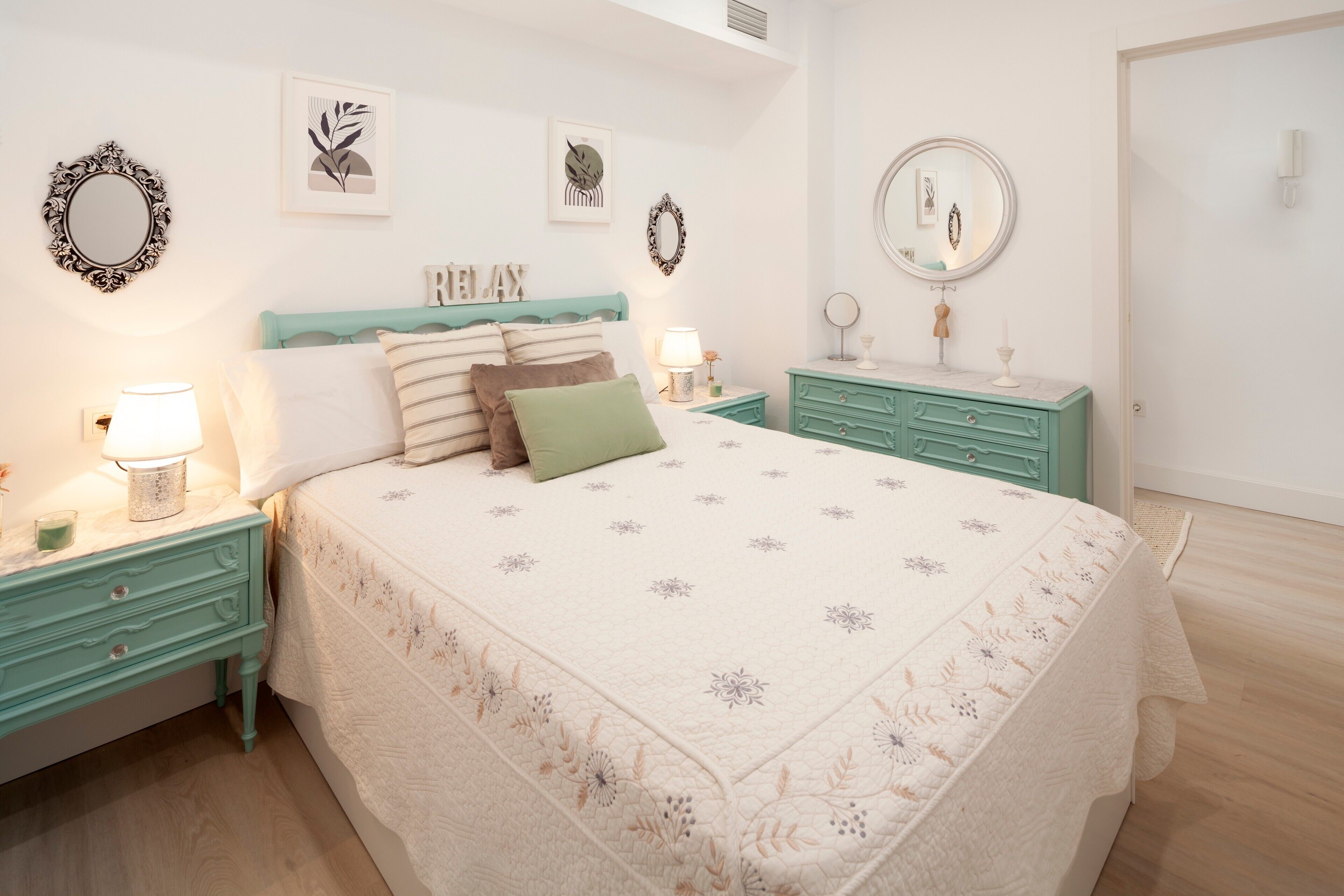 Un dormitorio con cama, dos mesitas de noche, cómoda, espejo y decoración en la pared.