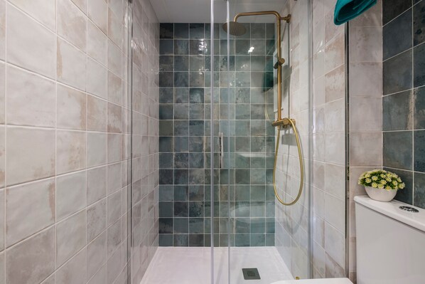 A shower with a glass door, a gold showerhead, and a white sink with a flower bowl.