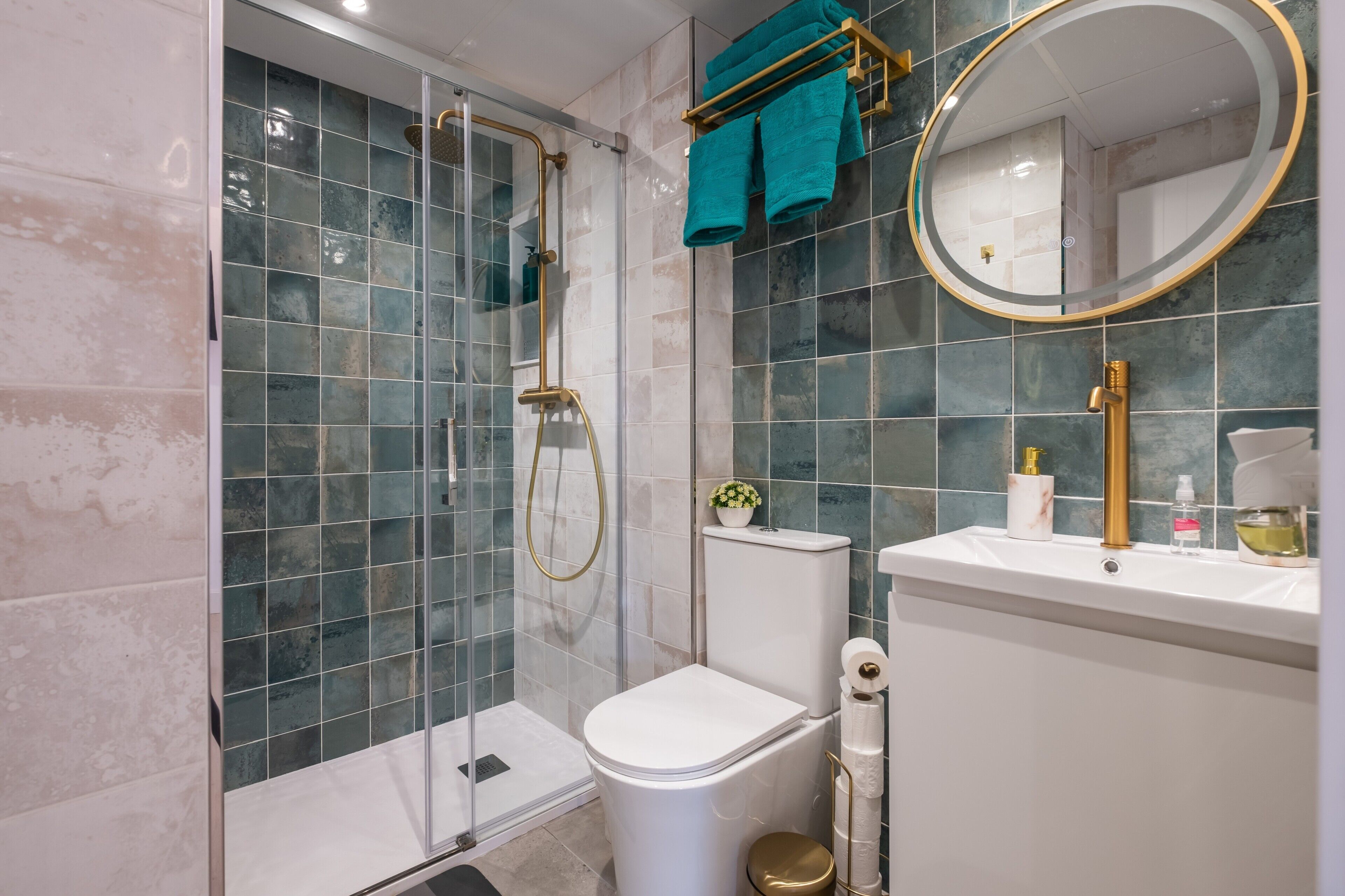 A modern bathroom with a glass-enclosed shower, a toilet, and a sink with gold fixtures.