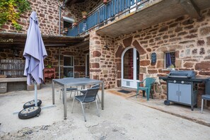 Un edificio de piedra con un balcón, una mesa con sillas, una parrilla y un toldo colgante.