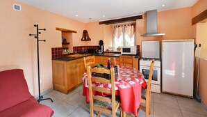 A compact kitchen with wooden cabinets, a dining table with chairs, a refrigerator, a microwave, and a stove. - Holiday Home "Gîte Le Pressoir Domaine de Jouani" with Shared Pool & A/C (villecomtal)