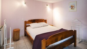 A bedroom with a wooden bed, a bedside table, a radiator, a wooden stool, and a wall-mounted light fixture. - Holiday Home "Gîte Le Pressoir Domaine de Jouani" with Shared Pool & A/C (villecomtal)
