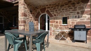An outdoor patio with a stone wall, a table with chairs, a small window, and a barbecue grill. - Holiday Home "Gîte Le Pressoir Domaine de Jouani" with Shared Pool & A/C (villecomtal)