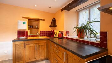 Una cocina con armarios de madera, un lavamanos empotrado, una ventana con una planta y un hervidor rojo.
