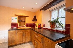 Una cocina con armarios de madera, un lavamanos empotrado, una ventana con una planta y un hervidor rojo.