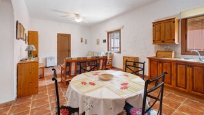 Ein Essbereich mit rundem Tisch, Stühlen, einem Deckenventilator und einer Küche mit Holzausstattung und einem Fenster.